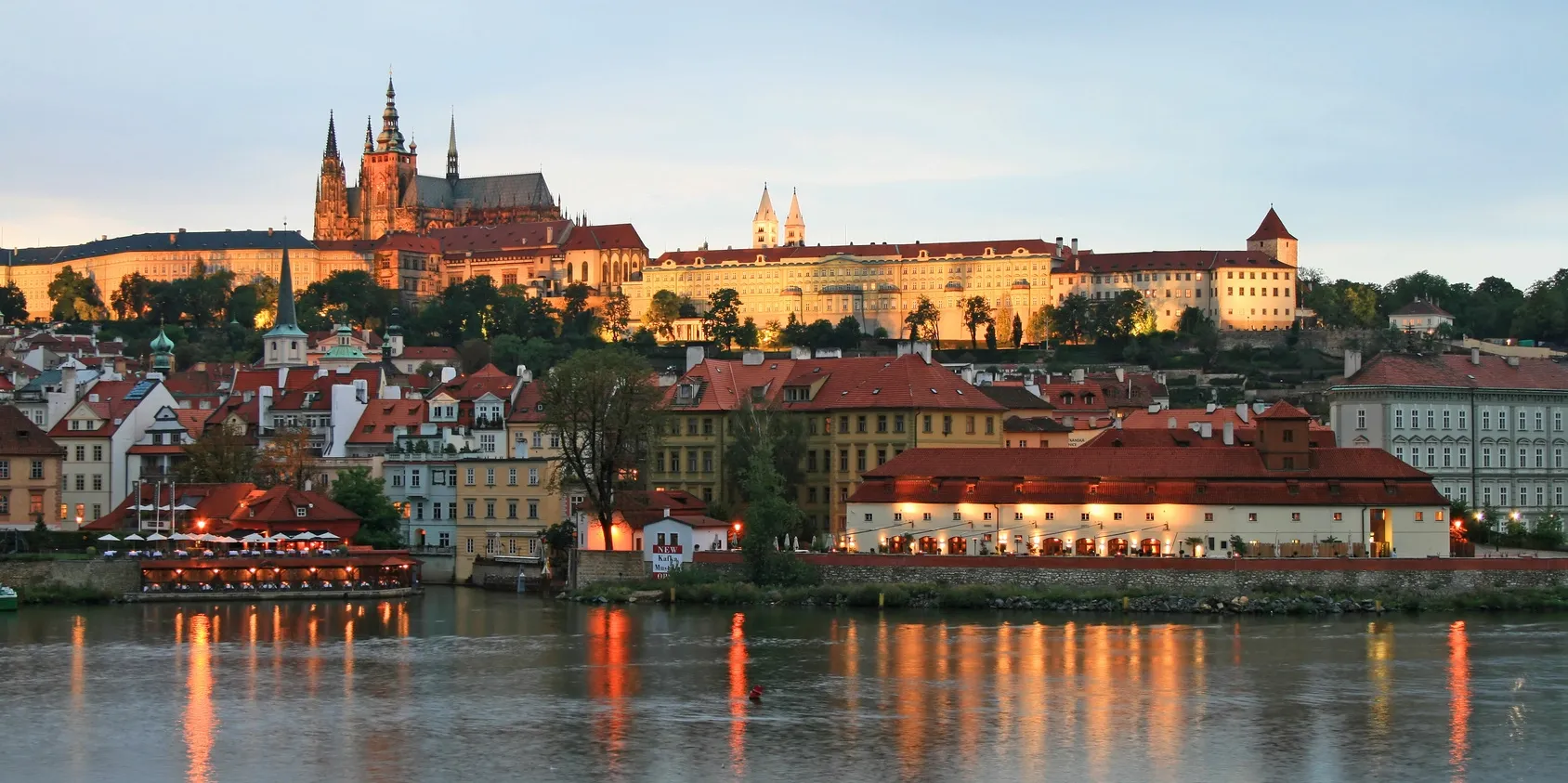 Prague Castle and the Vltava river in warm evening light.